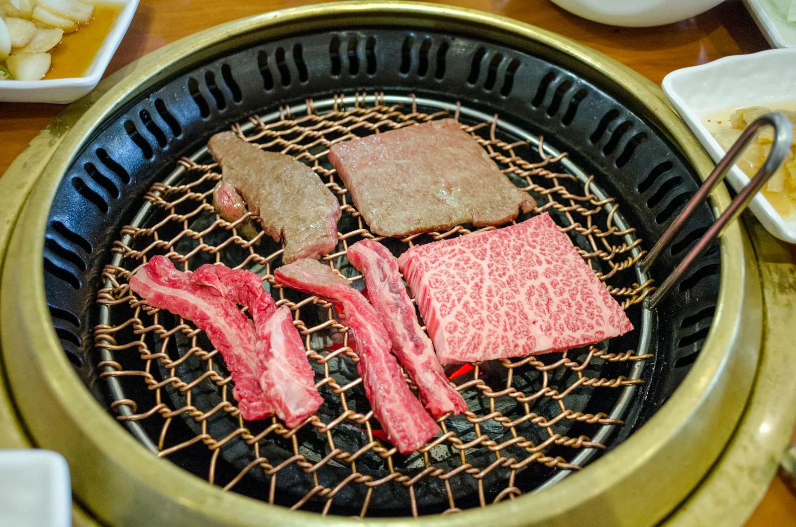Close-up Korean BBQ grill with meat cooking, used to explain beef and pork cut choices.
