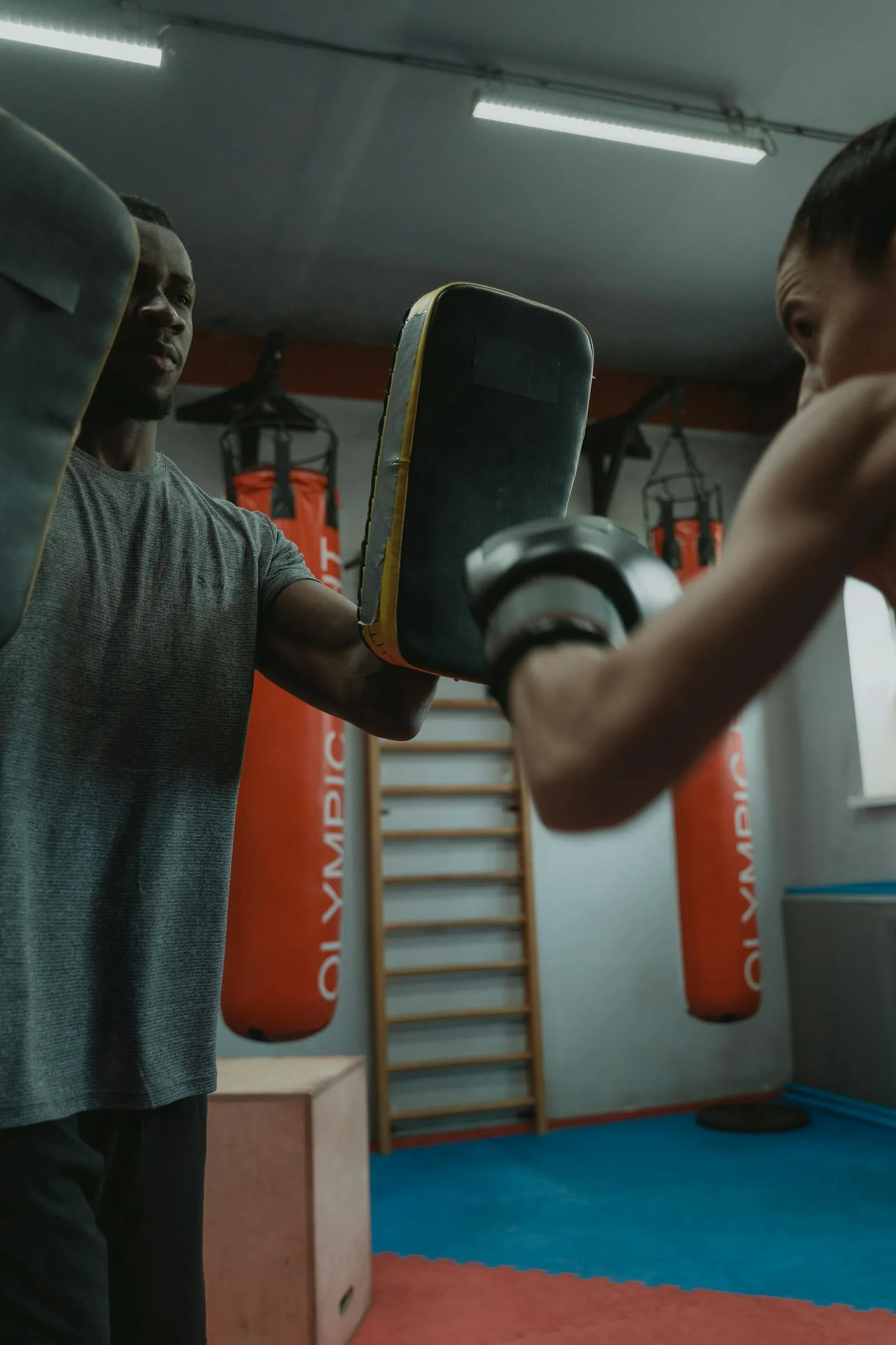 Boxing coach holding focus mitts during a beginner training session.
