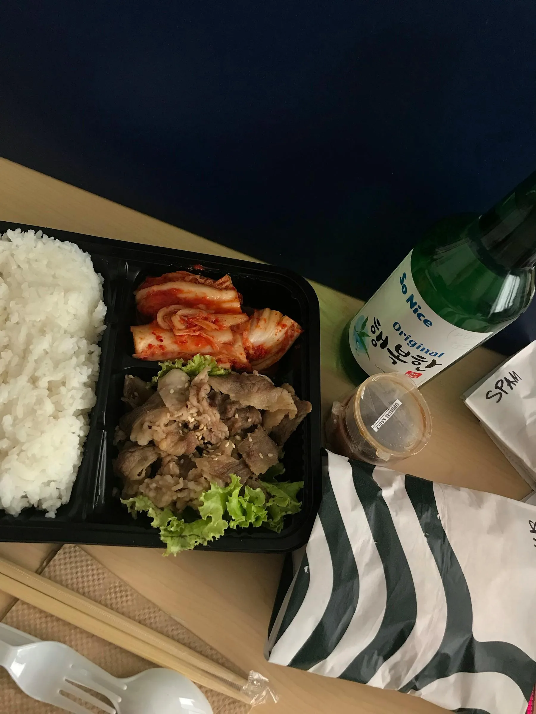 Top view of a Korean meal box with rice, side dishes, and drink.