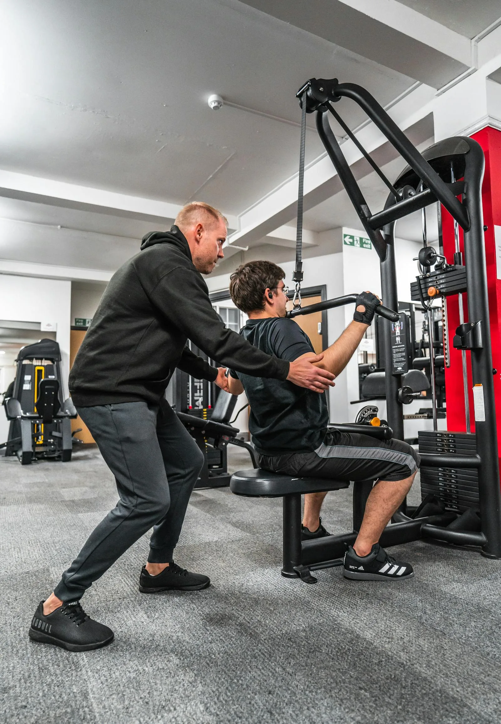 Personal trainer guiding a client on a gym machine, used to show clear coaching and instruction.