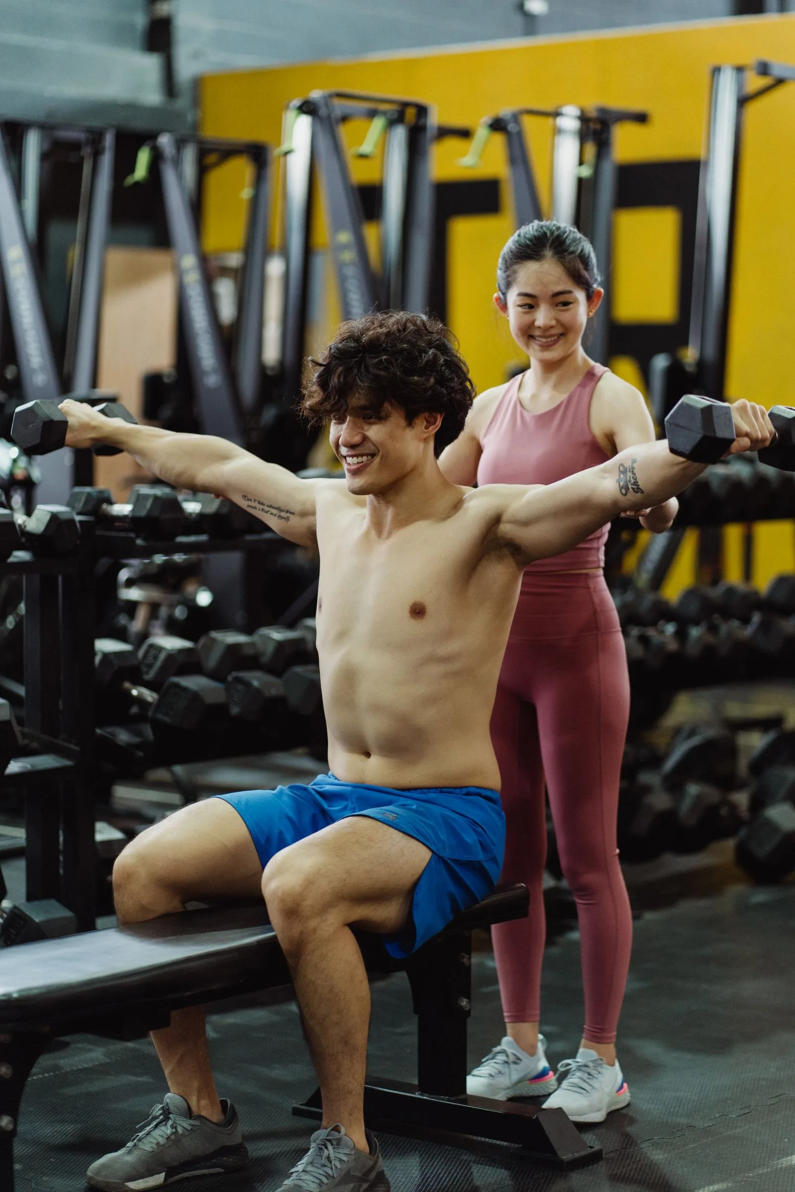 Personal trainer assisting a client with dumbbells in a gym.