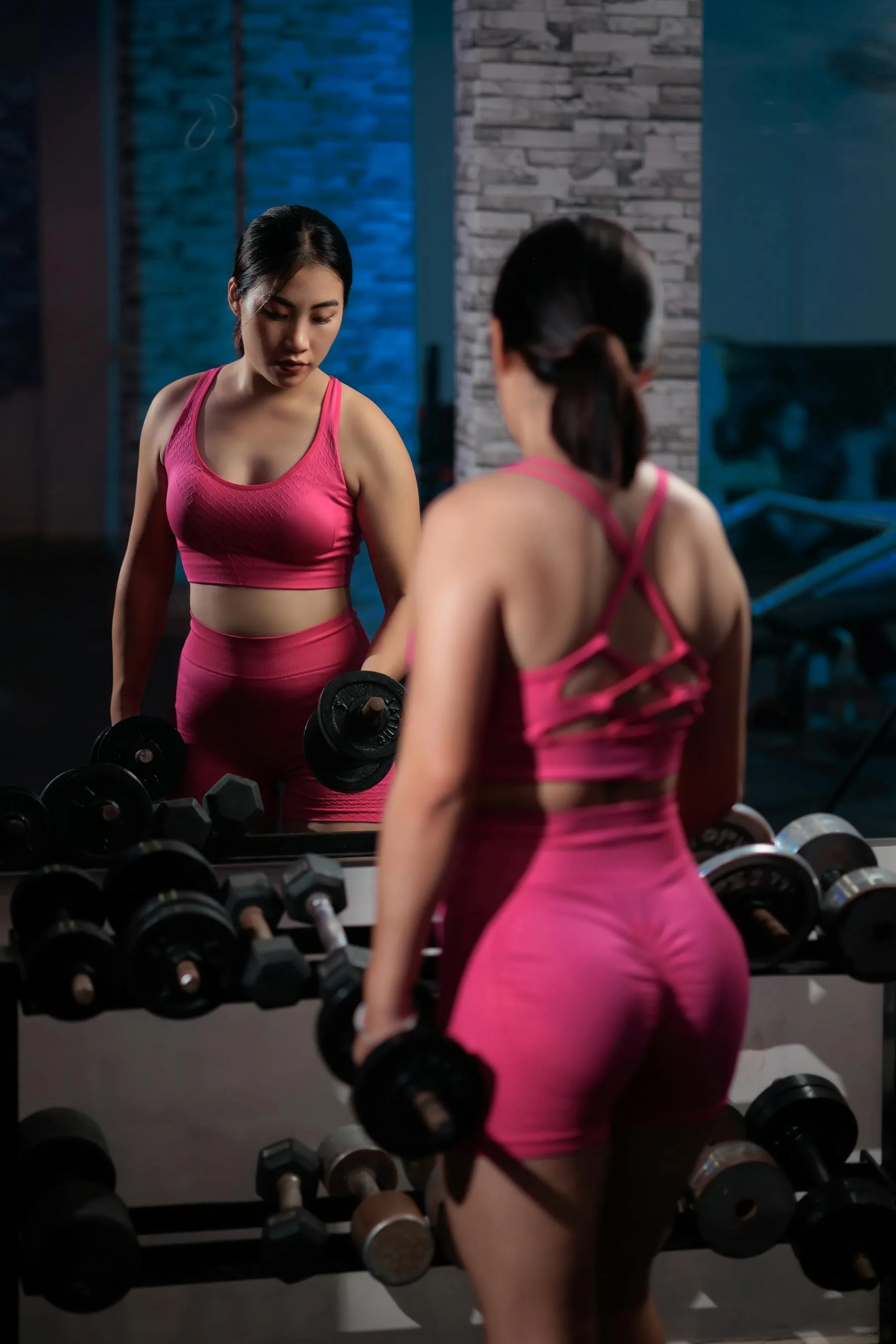 Woman lifting dumbbells in front of a gym mirror.