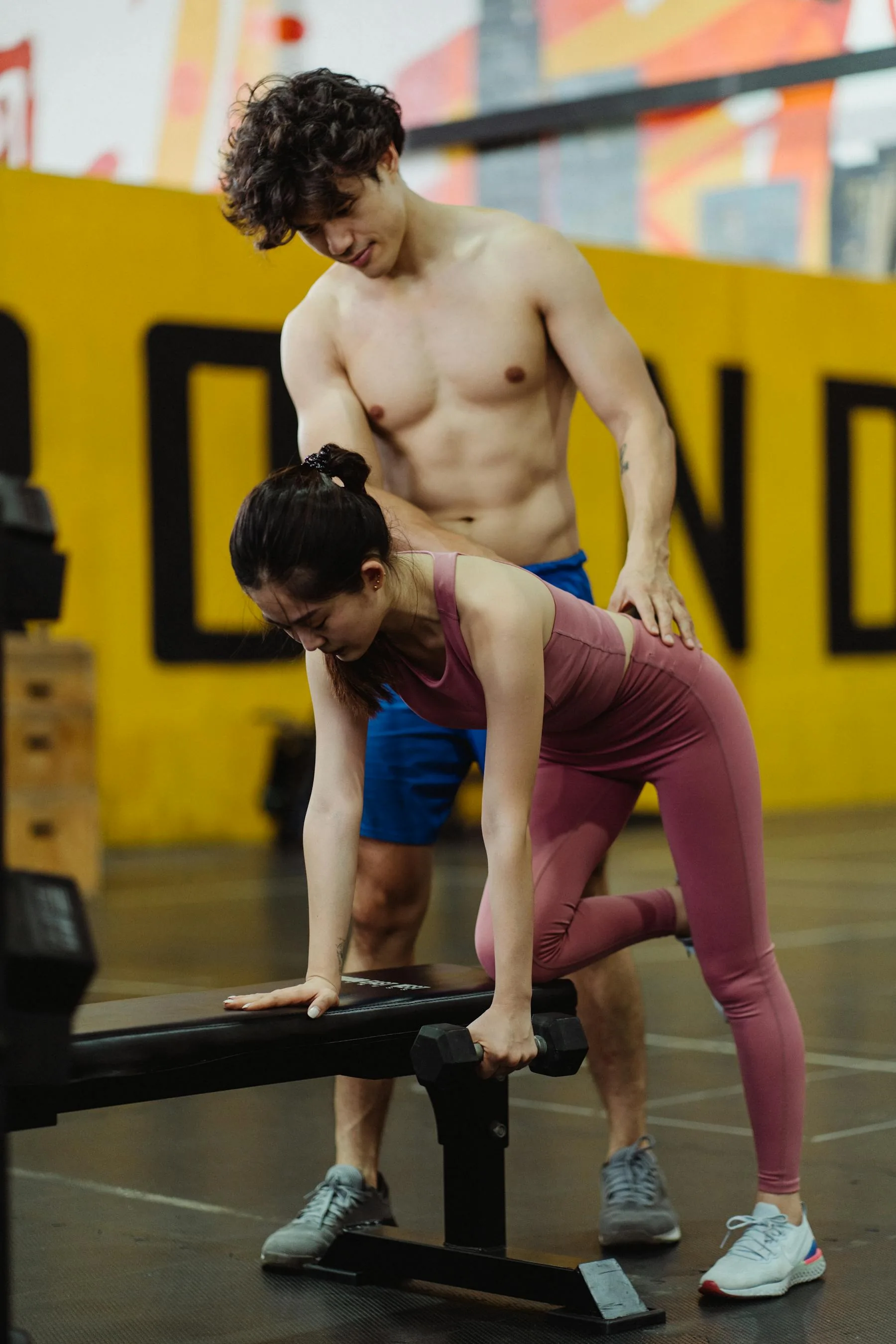 Trainer helping a client with weights during a coached gym session.