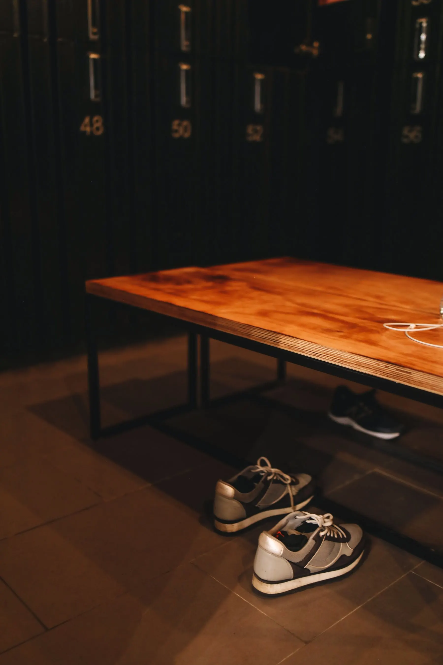 Training shoes placed beneath a bench beside numbered gym lockers.