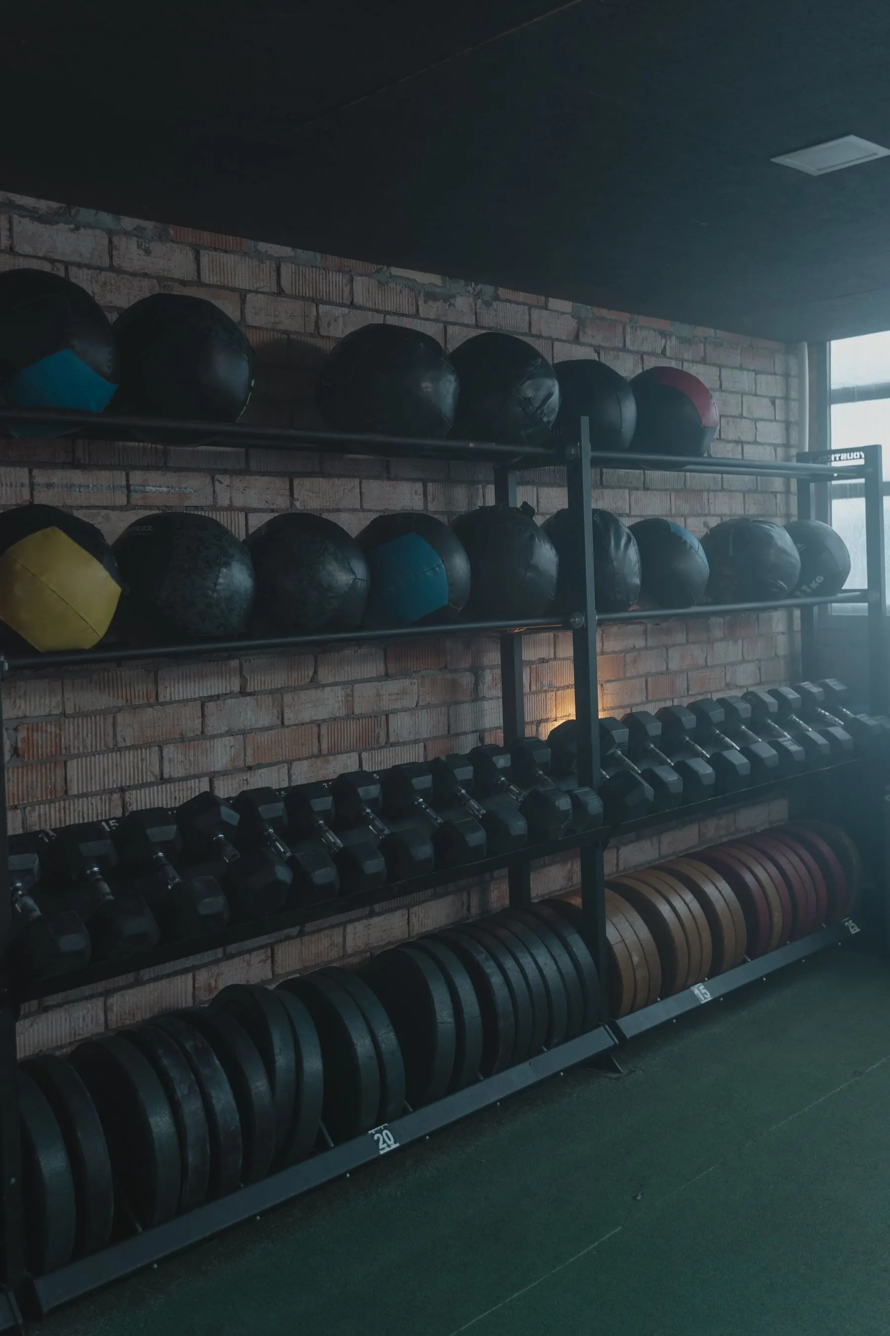 Dumbbells, medicine balls, and weight plates returned to an organized equipment rack.