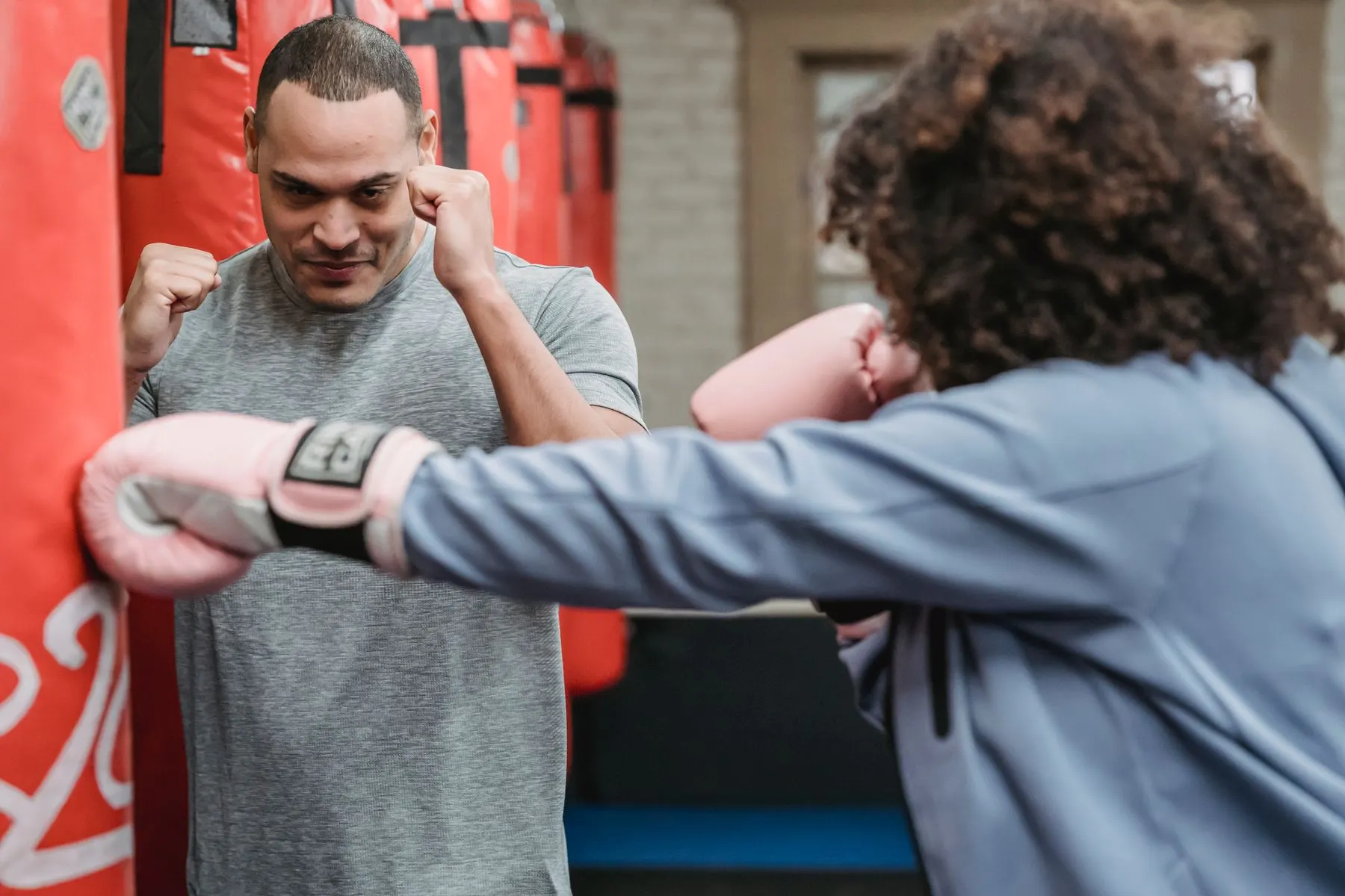 A coach demonstrating stance and positioning to a boxer beside a heavy bag.