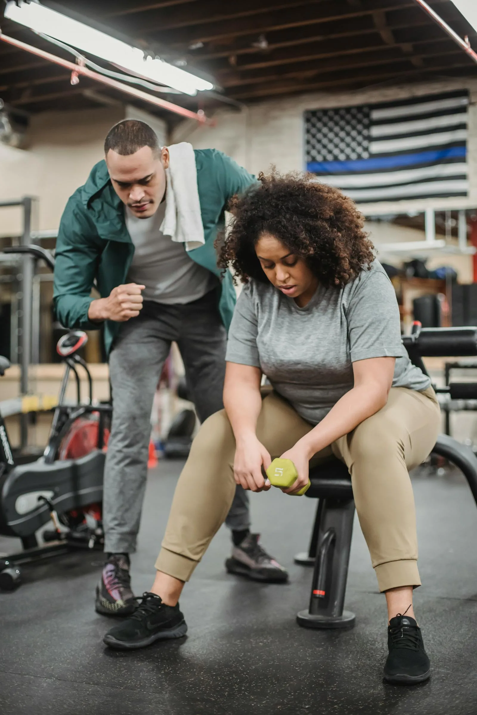 Trainer helping a client exercise with a dumbbell in a gym.