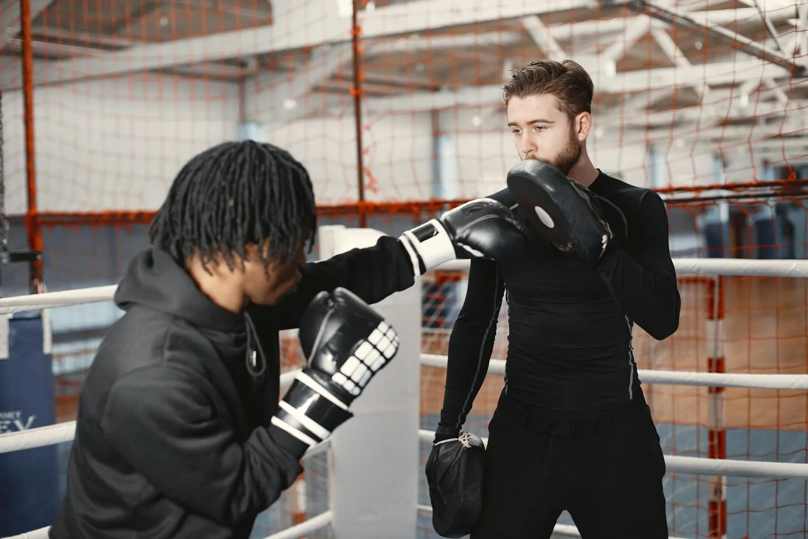 Boxing coach and trainee practicing padwork in a ring.