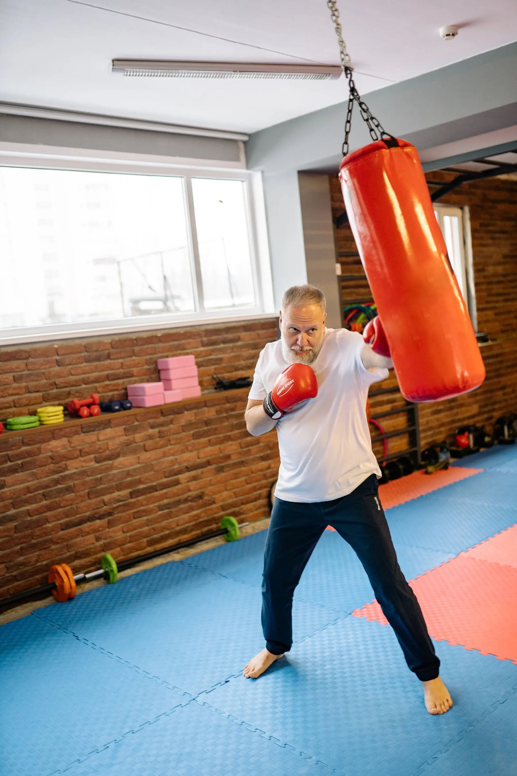 Older adult practising controlled boxing on a heavy bag in a bright gym.