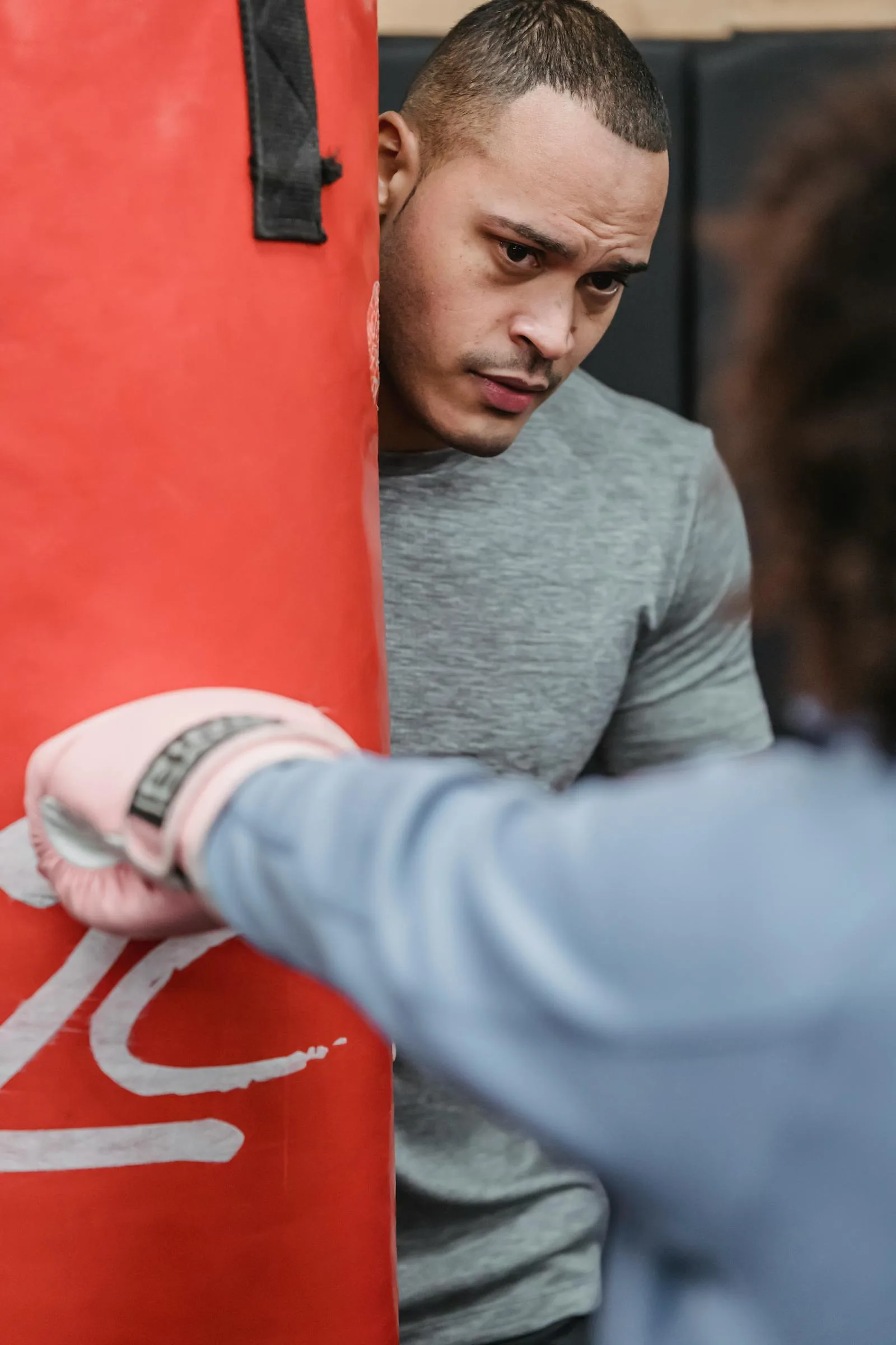 Boxing coach watching a trainee work on the punching bag.