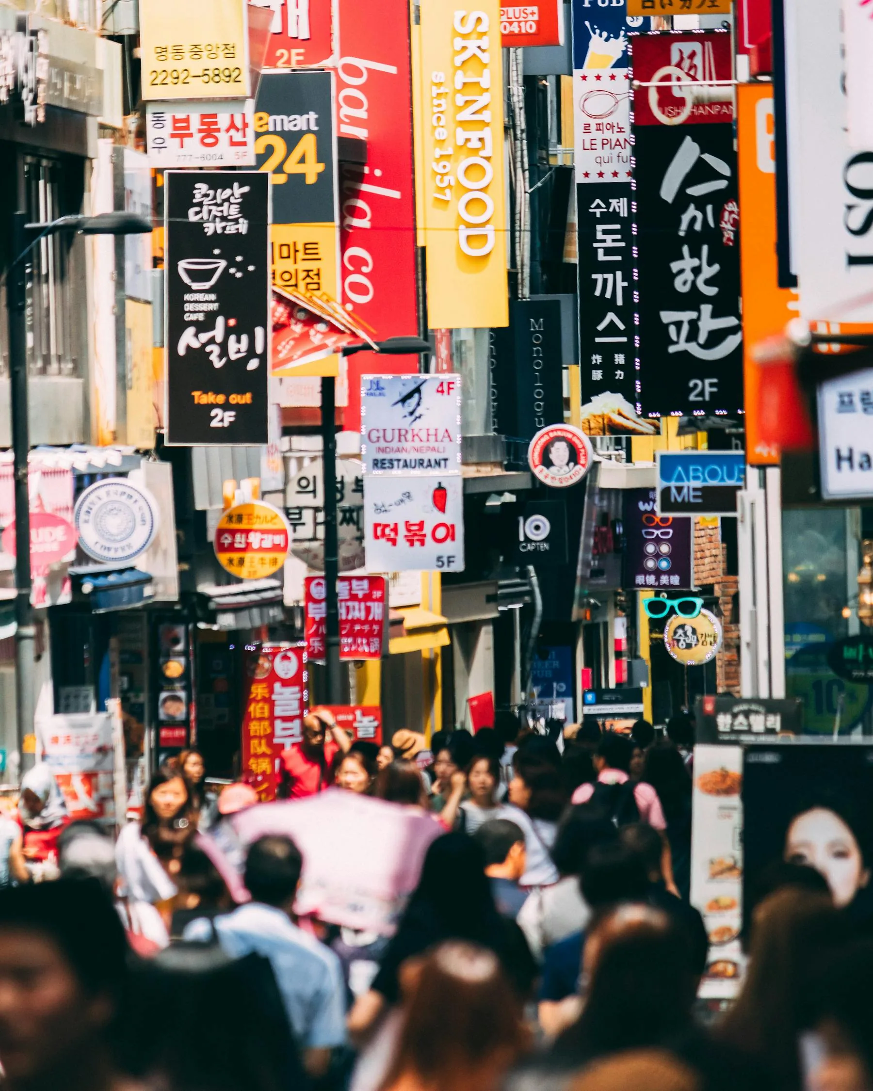 Crowded Korean shopping street with colorful signs and pedestrians.